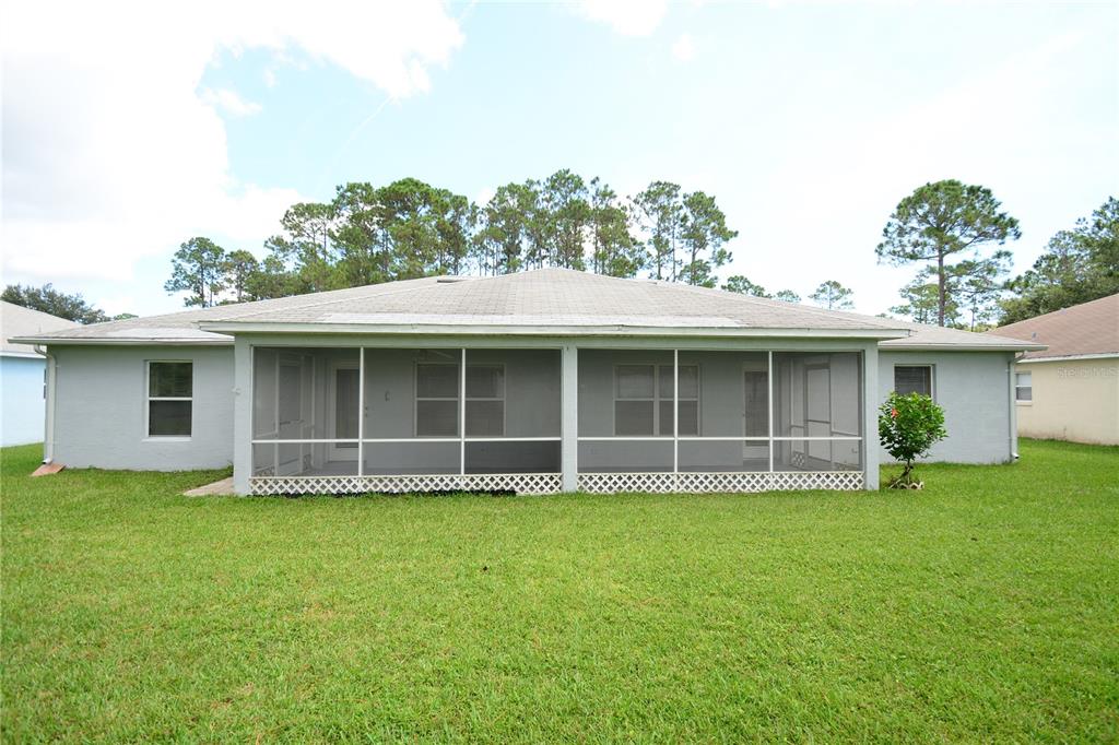 The back exterior of a single-story house features a large screened-in porch and lawn — 37 ETON LANE UNIT B, PALM COAST, FL