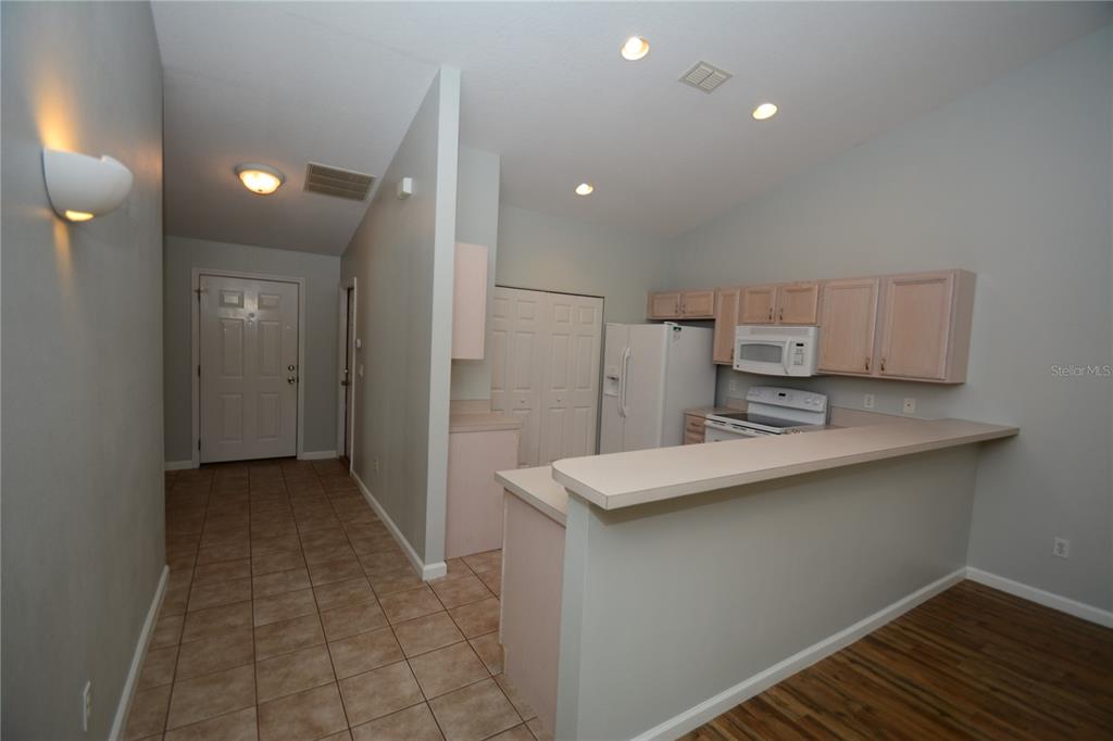 A kitchen with light wood cabinets, white appliances, and a breakfast bar overlooks a tiled entryway — 37 ETON LANE UNIT B, PALM COAST, FL