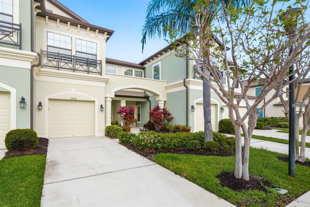 A two-story townhouse exterior features a beige garage, a covered entryway, and green siding — 11636 CROWNED SPARROW LANE, TAMPA, FL