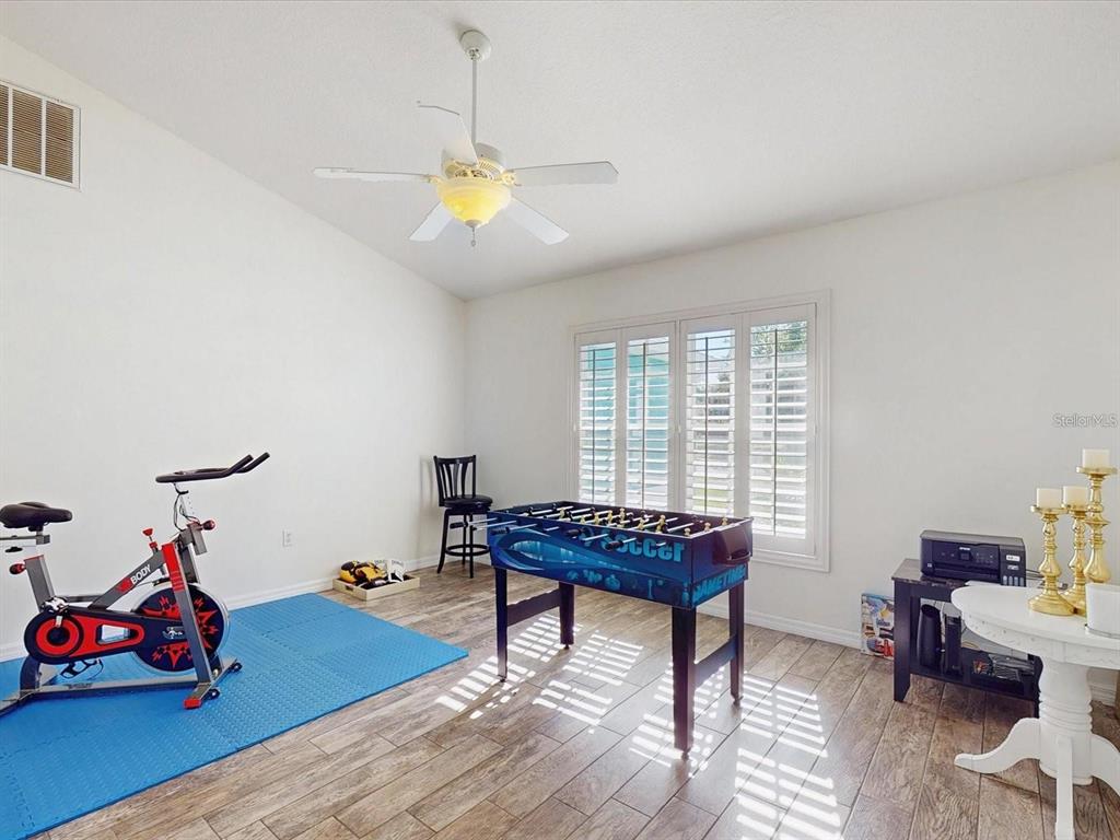A room with wood-look tile flooring, a ceiling fan, a stationary bike, and a foosball table — 2211 JESSICA LANE, KISSIMMEE, FL