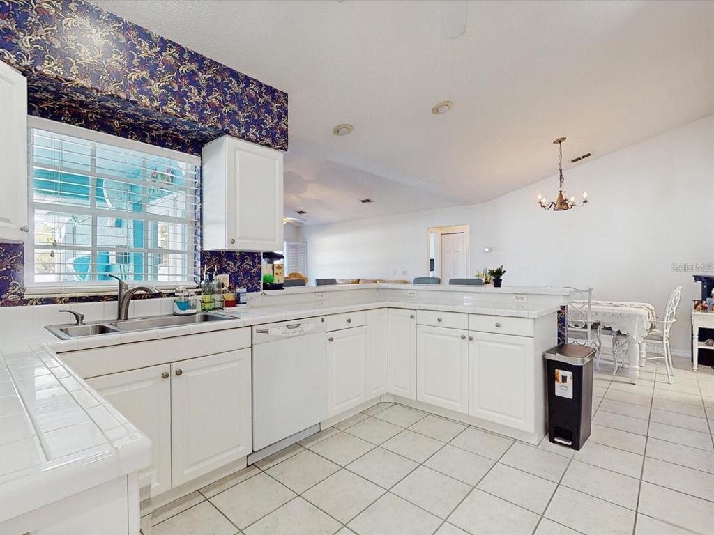 A white kitchen with tile countertops and patterned wallpaper above the sink window — 2211 JESSICA LANE, KISSIMMEE, FL
