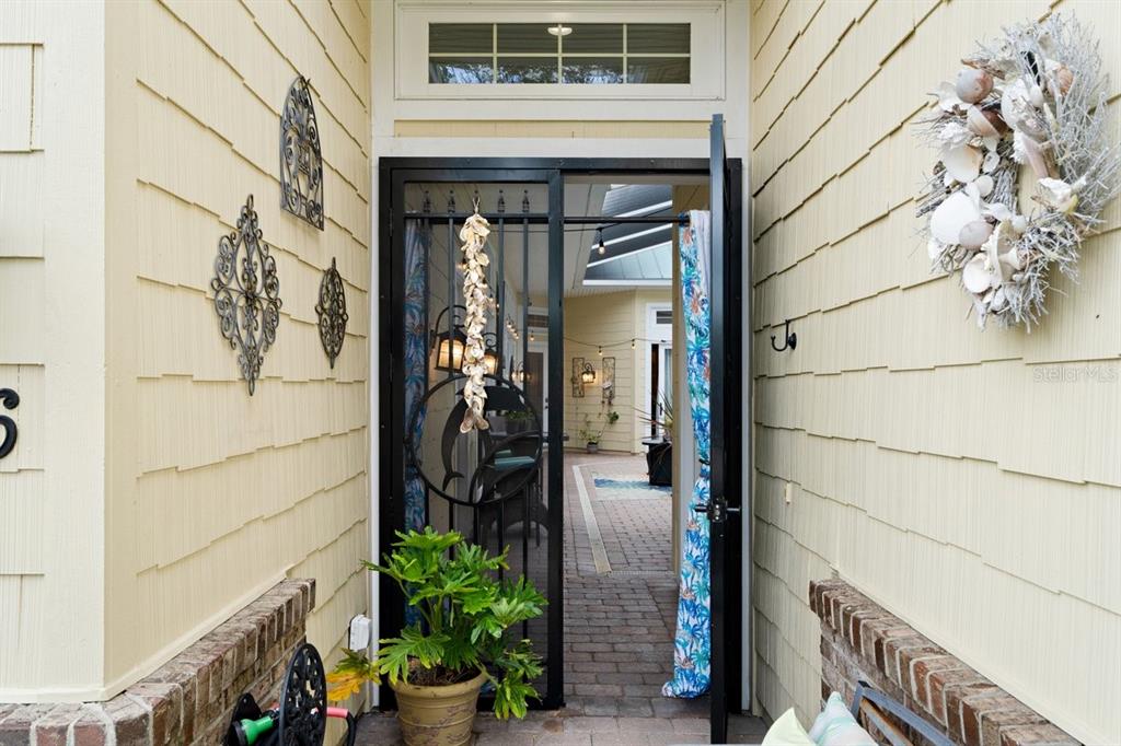 An open black metal screen door leads into a paved courtyard with light yellow siding — 4606 OAK HAMMOCK COURT UNIT 4606, PONCE INLET, FL