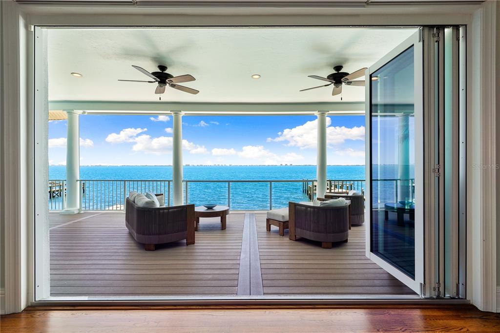 A covered deck with lounge furniture overlooks the ocean through large folding glass doors — 350 S SHORE DRIVE, SARASOTA, FL