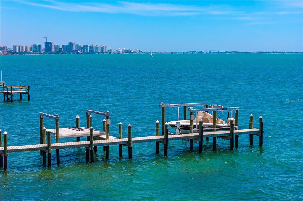 A wooden dock with a boat lift extends into a bay with a city skyline — 350 S SHORE DRIVE, SARASOTA, FL