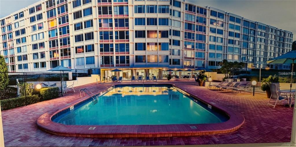 A rectangular swimming pool sits on a brick patio in front of a large apartment building — 700 MIRROR TERRACE NW UNIT 507, WINTER HAVEN, FL