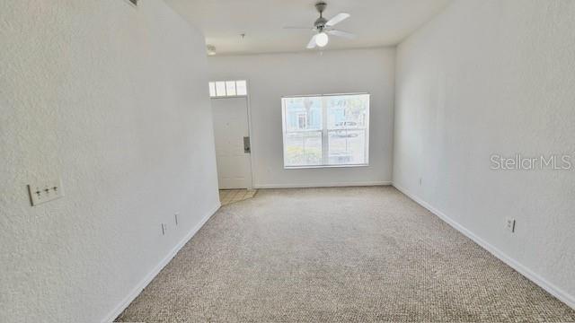 An empty living room features beige carpeting, white walls, a ceiling fan, and a front door — 2219 SAN VITTORINO CIRCLE UNIT 106, KISSIMMEE, FL