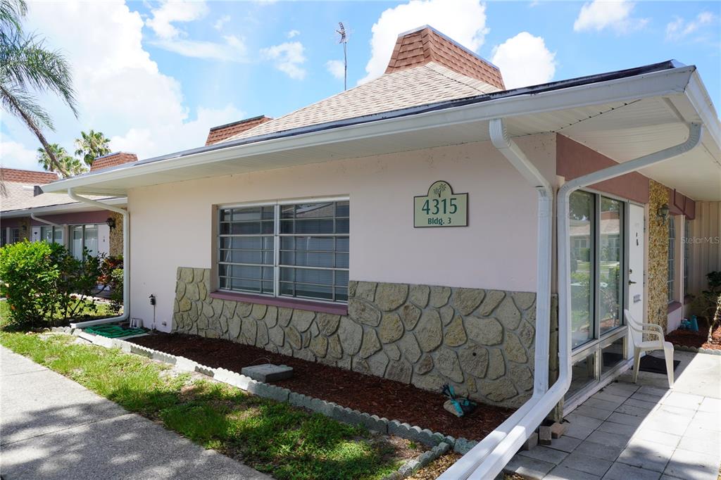 A single-story building exterior features pink stucco walls, stone accents, and a shingled roof — 4315 TAHITIAN GARDENS CIRCLE UNIT H, HOLIDAY, FL