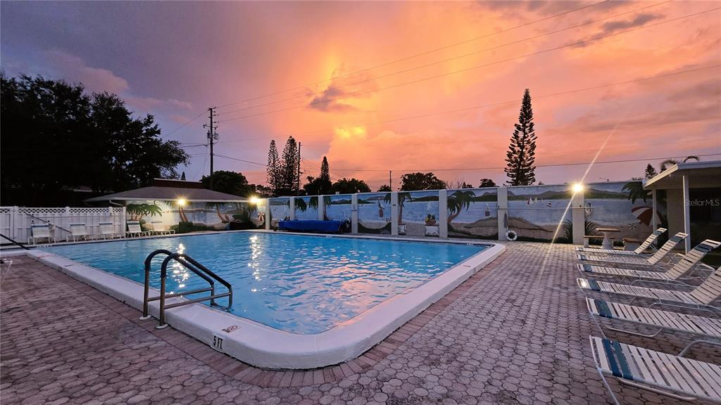 A swimming pool with lounge chairs on a brick deck under a sunset sky — 4315 TAHITIAN GARDENS CIRCLE UNIT H, HOLIDAY, FL