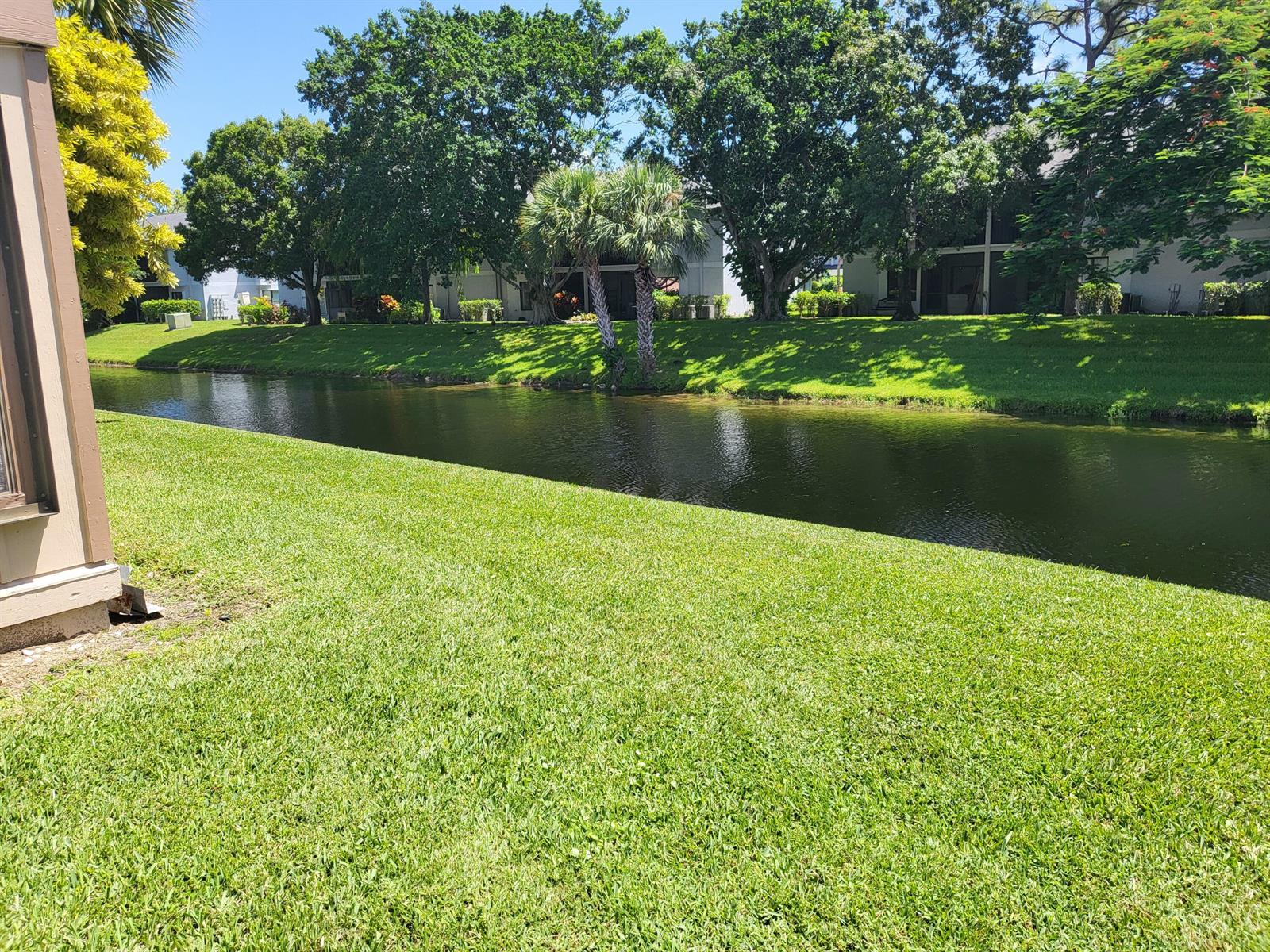 A grassy lawn overlooks a narrow canal with trees and residential buildings in the background — 500 Crosswinds Drive # F1, FL 33413, FL