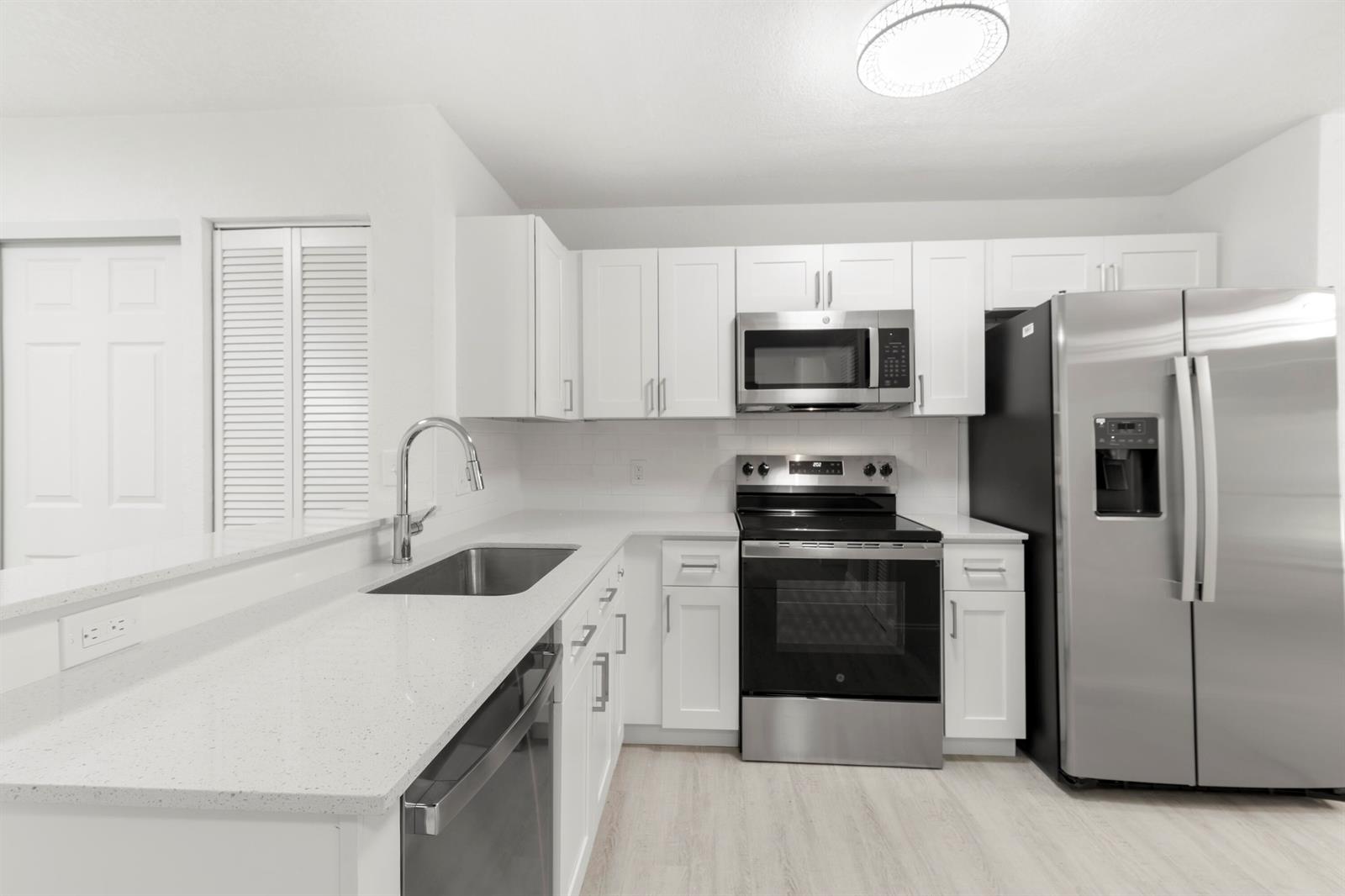 A modern kitchen features white cabinets, stainless steel appliances, and light-colored quartz countertops — 500 Crosswinds Drive # F1, FL 33413, FL