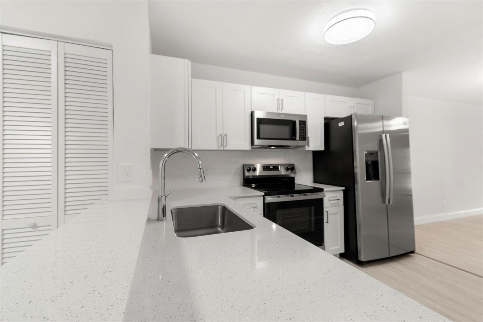 A kitchen features white cabinets, quartz countertops, stainless steel appliances, and a modern light fixture — 500 Crosswinds Drive # F1, FL 33413, FL