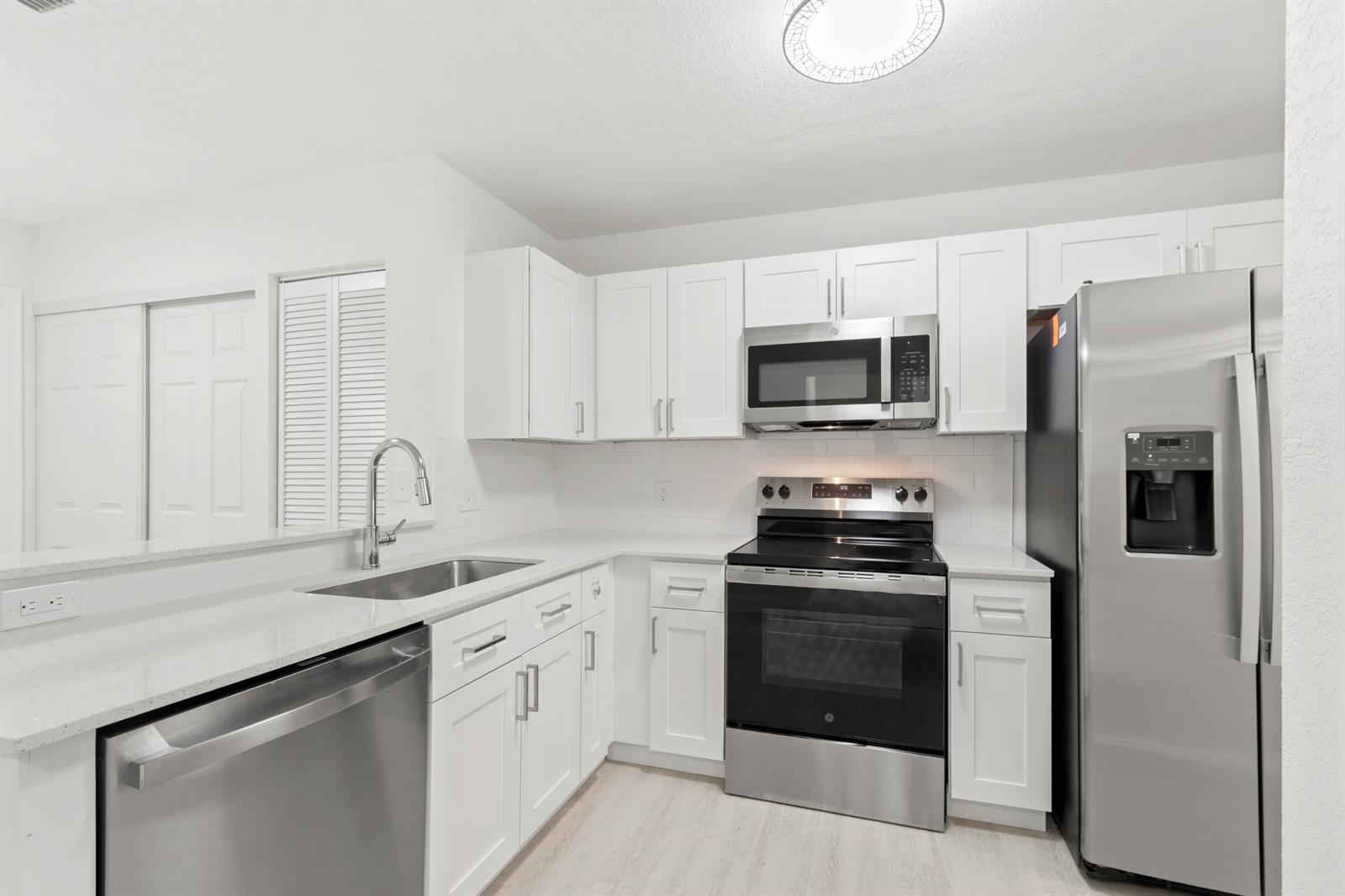 A kitchen features white cabinets, stainless steel appliances, quartz countertops, and a subway tile backsplash — 500 Crosswinds Drive # F1, FL 33413, FL