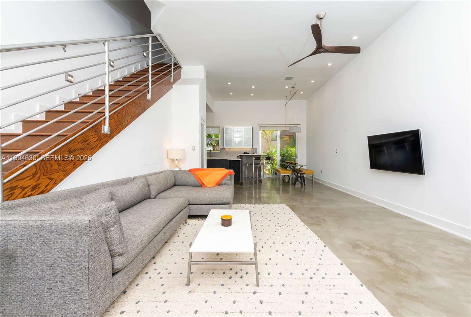 A modern living room features a gray sectional sofa, concrete floors, and a wooden staircase — 361 Jefferson Ave # 3, Miami Beach FL 33139, MIAMI BEACH, FL