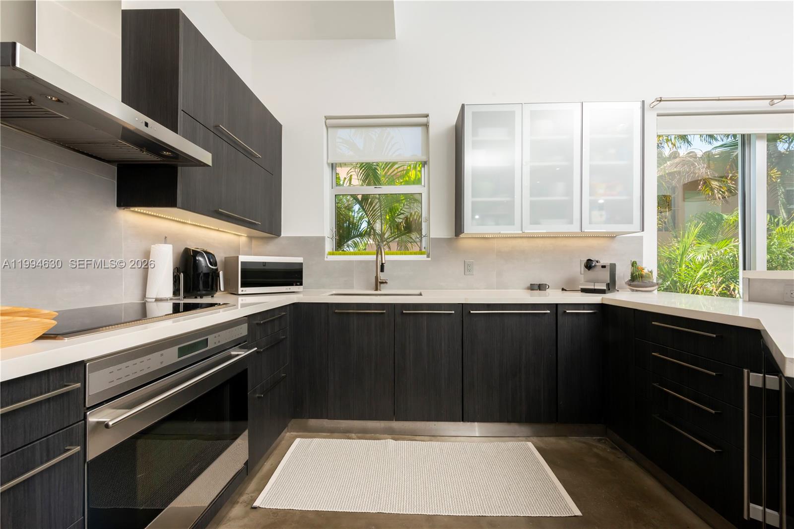 A modern kitchen features dark wood cabinetry, white countertops, stainless steel appliances, and a window — 361 Jefferson Ave # 3, Miami Beach FL 33139, MIAMI BEACH, FL