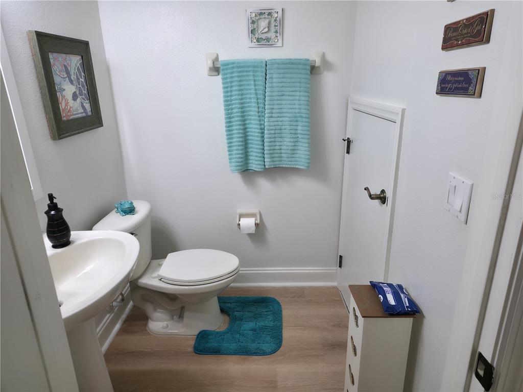 A small bathroom features a pedestal sink, toilet, light wood flooring, and a small storage door — 14742 CLARKSON DRIVE, ORLANDO, FL