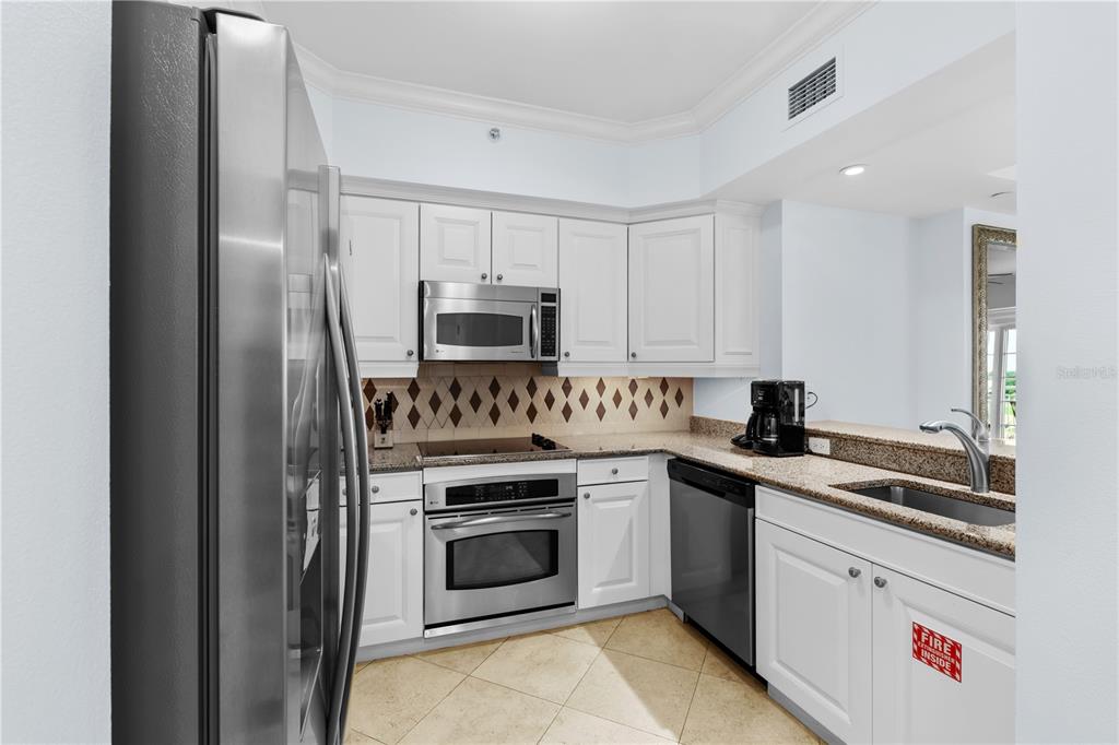 A kitchen features white cabinets, stainless steel appliances, granite countertops, and a tile floor — 7593 GATHERING DRIVE UNIT 706, KISSIMMEE, FL