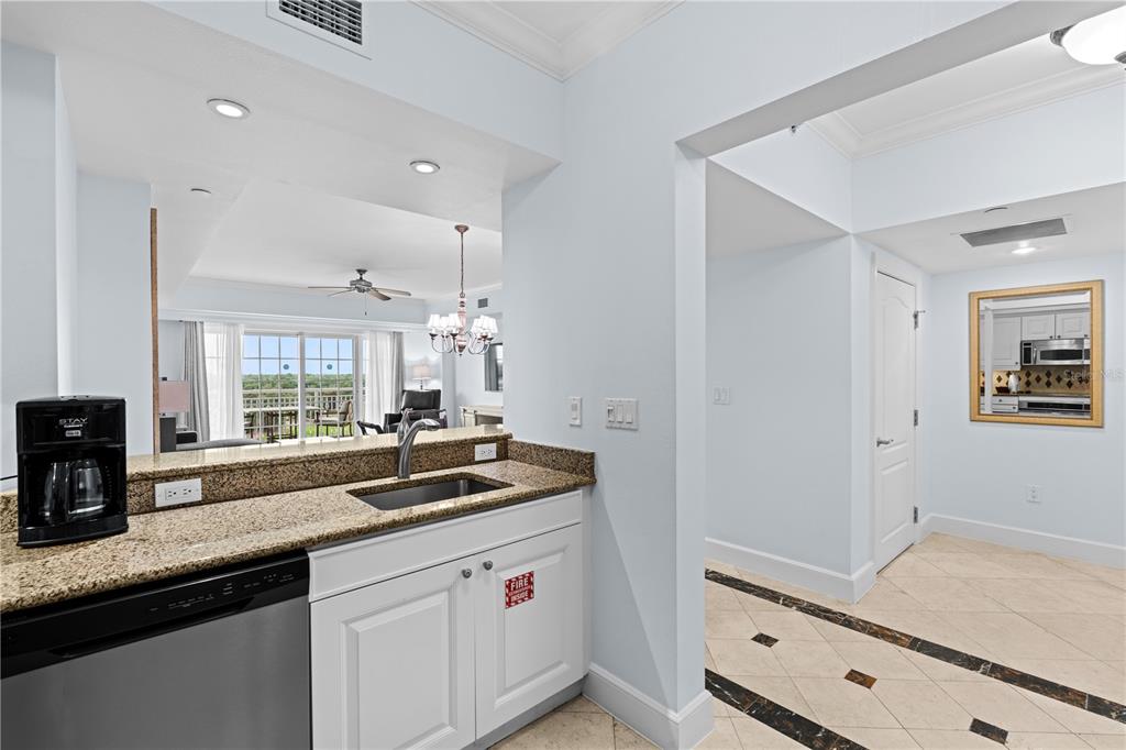 A kitchen with granite countertops and stainless steel appliances overlooks a living area with balcony access — 7593 GATHERING DRIVE UNIT 706, KISSIMMEE, FL