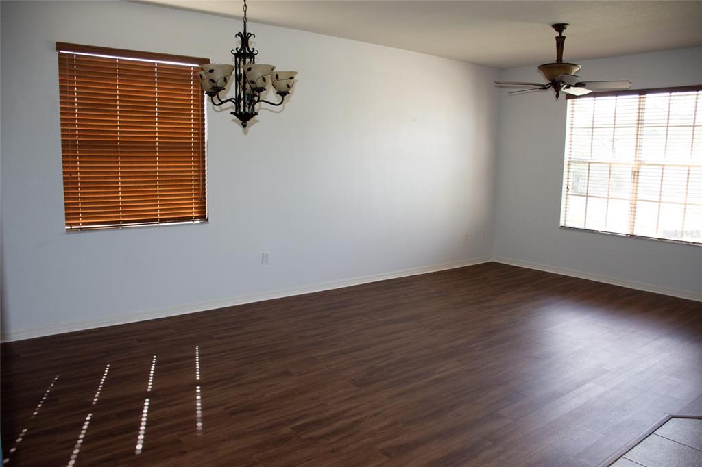 An empty room features dark wood-look flooring, a chandelier, a ceiling fan, and two windows — 2504 LADOGA DRIVE, LAKELAND, FL