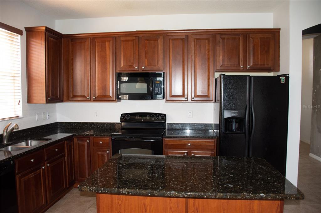 A kitchen features dark wood cabinets, black appliances, and granite countertops with a central island — 2504 LADOGA DRIVE, LAKELAND, FL