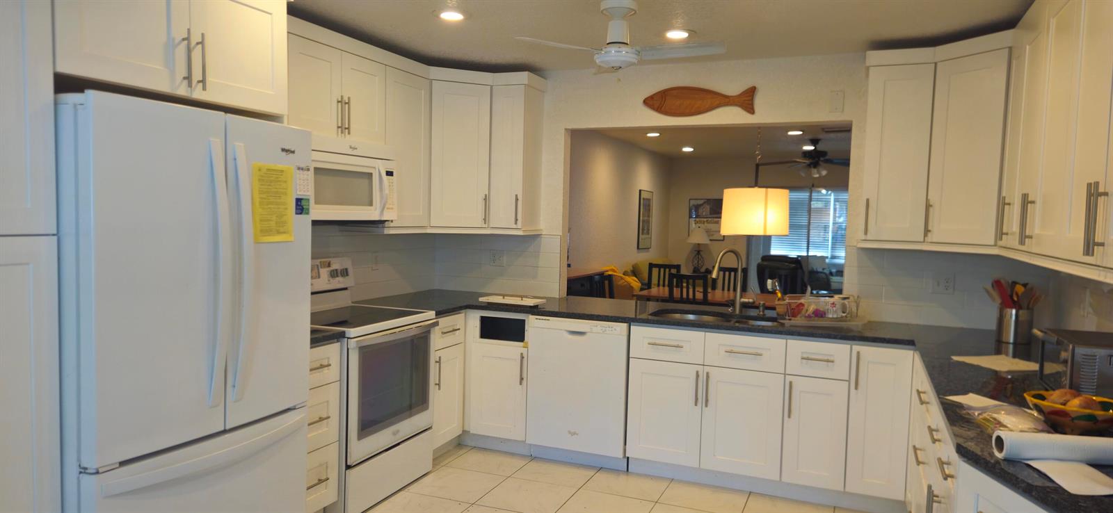 A kitchen features white cabinets, dark countertops, a white refrigerator, and a pass-through window — 5432 Privet Pl Place # D, Delray Beach FL 33484, DELRAY BEACH, FL