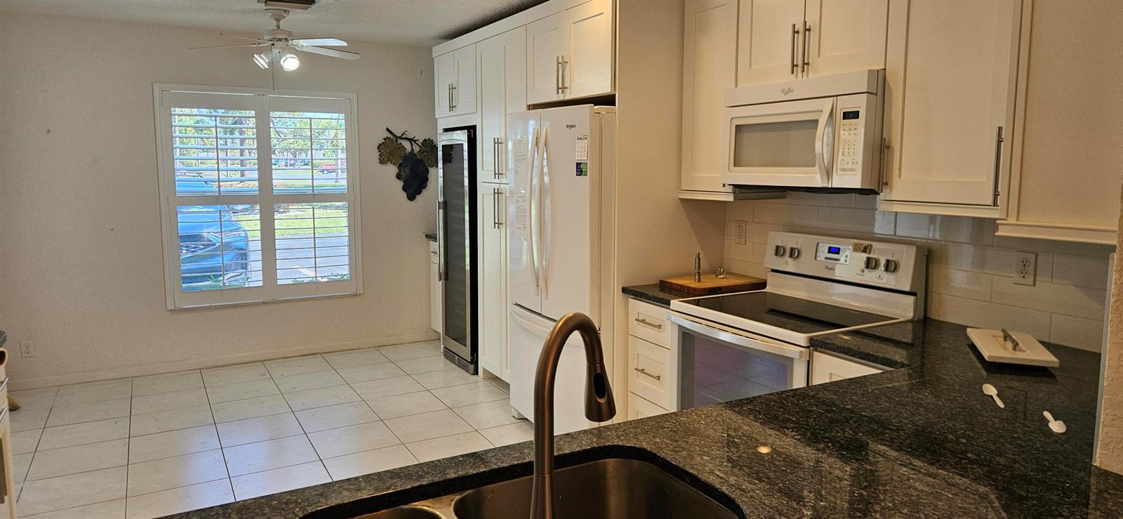 A kitchen features white cabinets, dark granite countertops, stainless steel appliances, and tile flooring — 5432 Privet Pl Place # D, Delray Beach FL 33484, DELRAY BEACH, FL
