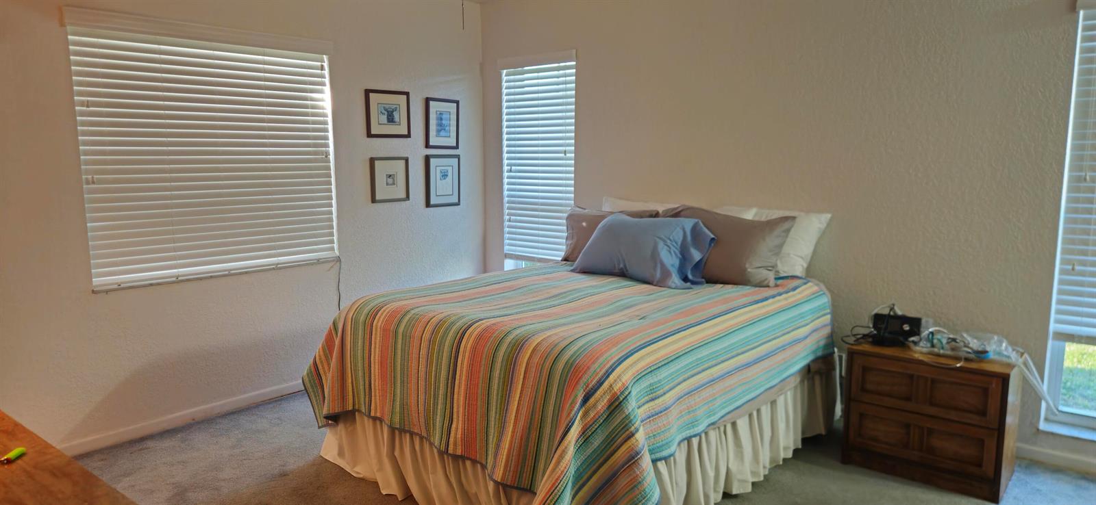 A bedroom features a striped quilt on the bed, a wooden nightstand, and two windows — 5432 Privet Pl Place # D, Delray Beach FL 33484, DELRAY BEACH, FL