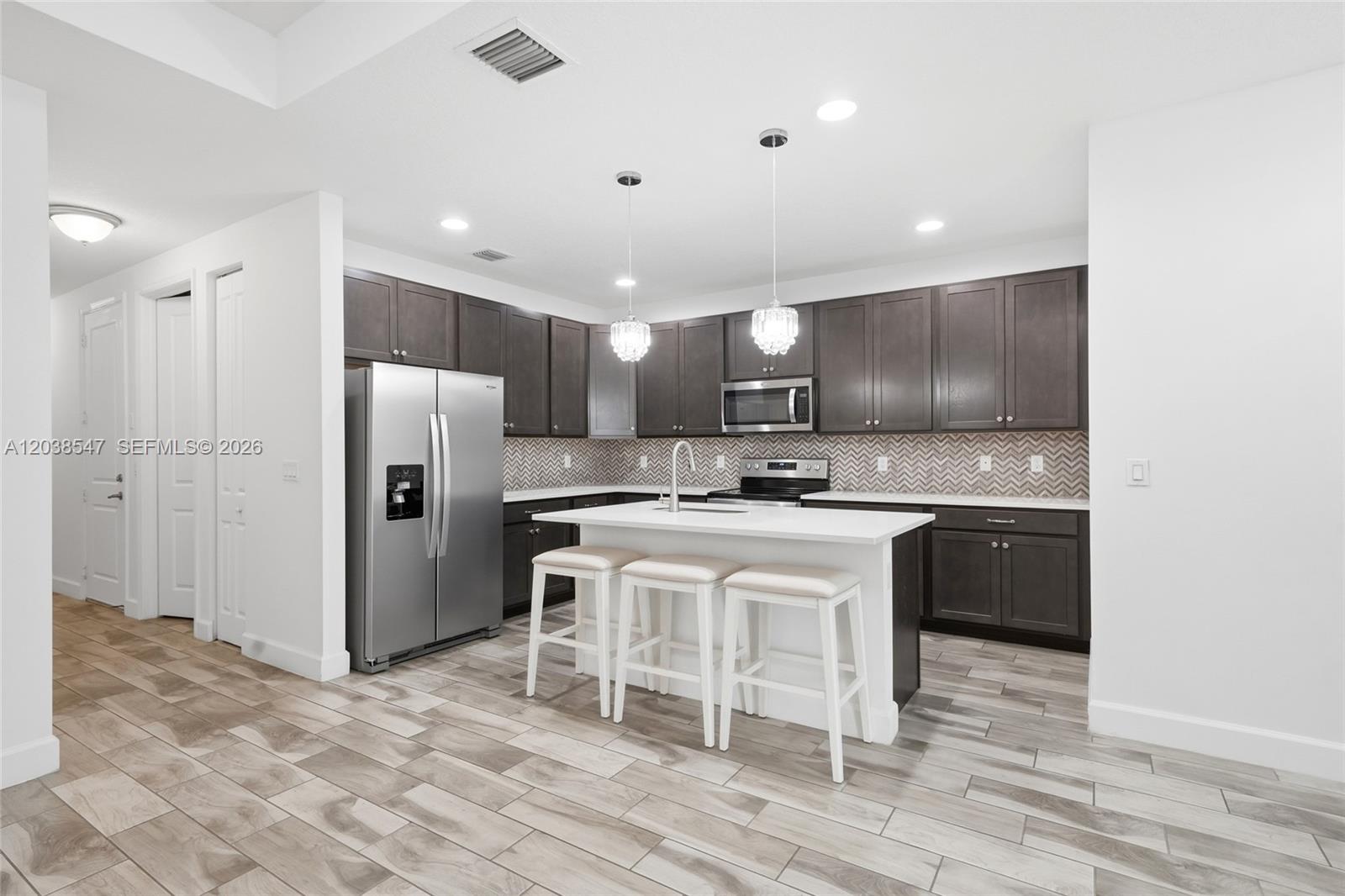 A modern kitchen features dark wood cabinets, stainless steel appliances, and a white island — 3384 NW 5th St, Pompano Beach FL 33069, POMPANO BEACH, FL