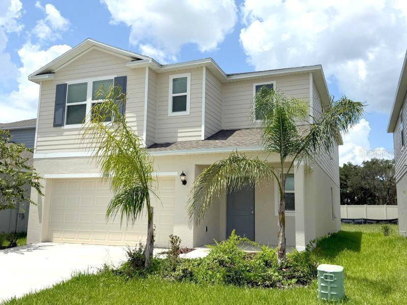 A two-story, beige suburban house features a two-car garage, a front door, and palm trees — 11893 NOBLE CHASE PATH, DADE CITY, FL