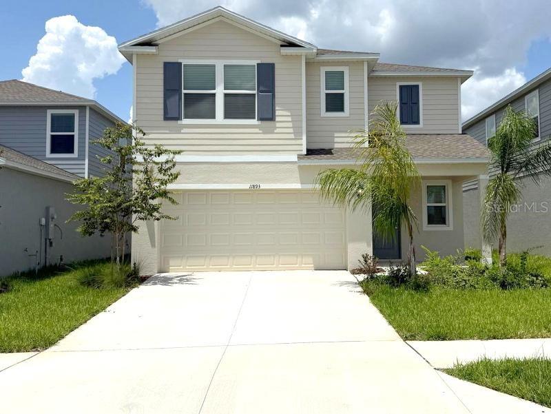 A two-story suburban house with beige siding, a two-car garage, and a concrete driveway — 11893 NOBLE CHASE PATH, DADE CITY, FL