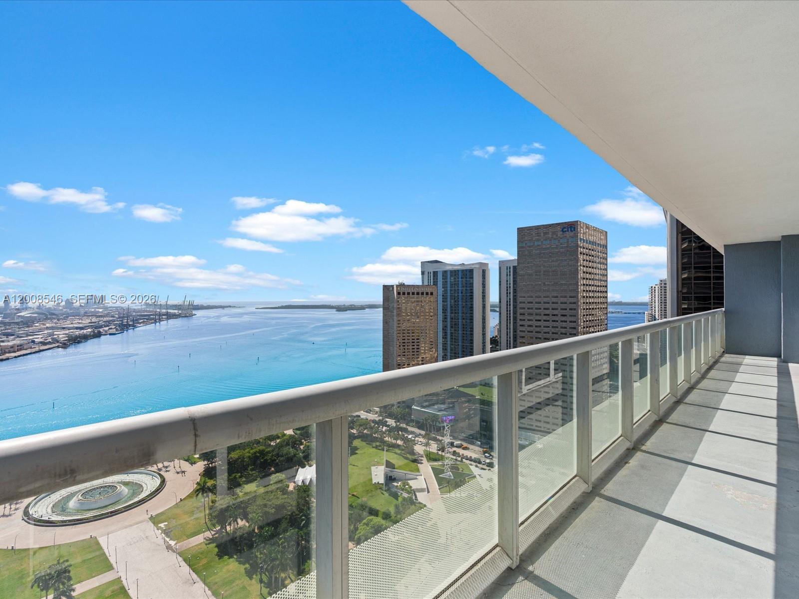 A high-rise balcony overlooks a park, a circular fountain, and a bay with skyscrapers — 50 Biscayne Blvd # 3308, Miami FL 33132, MIAMI, FL