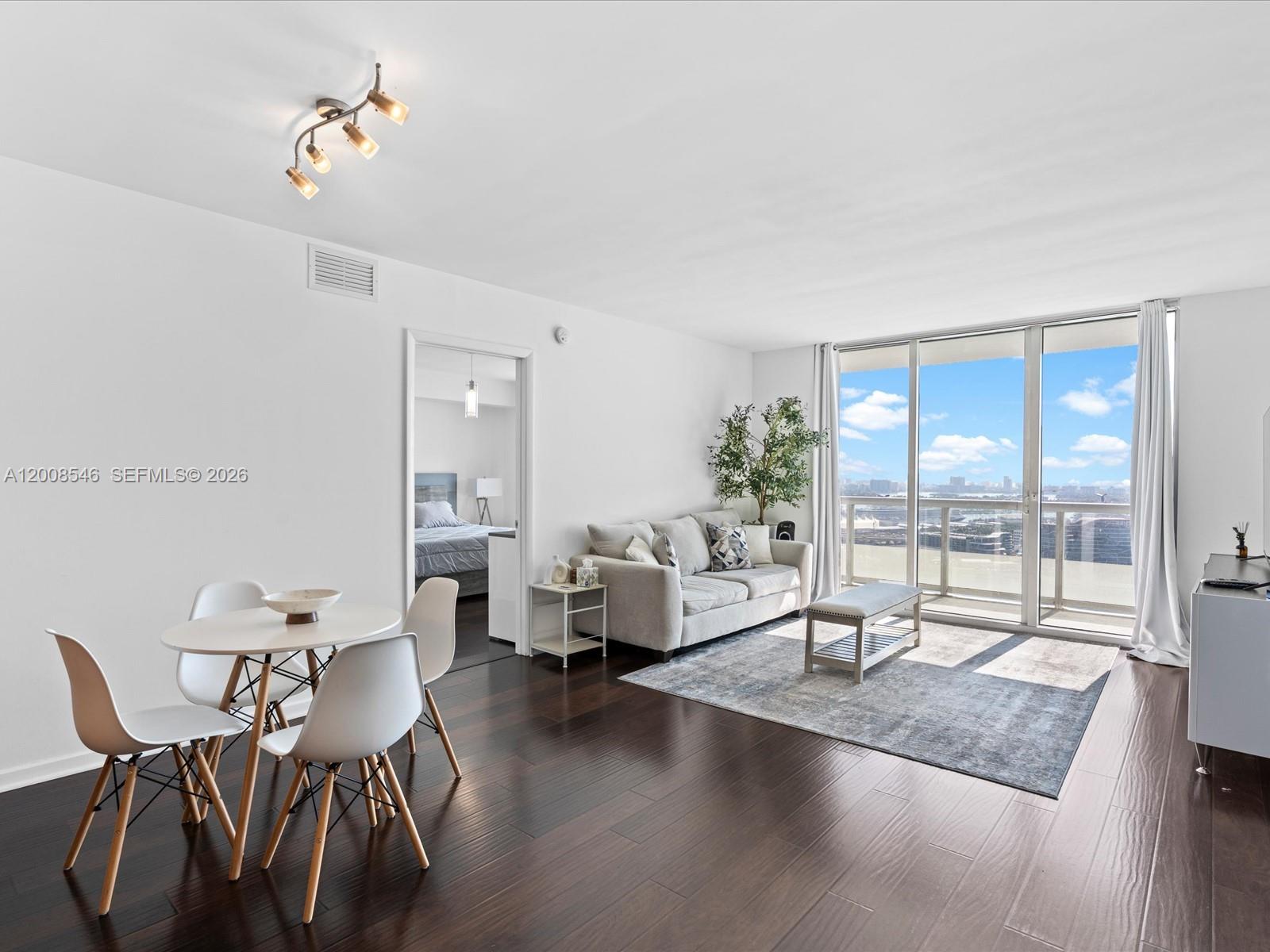A living and dining area features dark wood floors, white walls, and floor-to-ceiling windows — 50 Biscayne Blvd # 3308, Miami FL 33132, MIAMI, FL