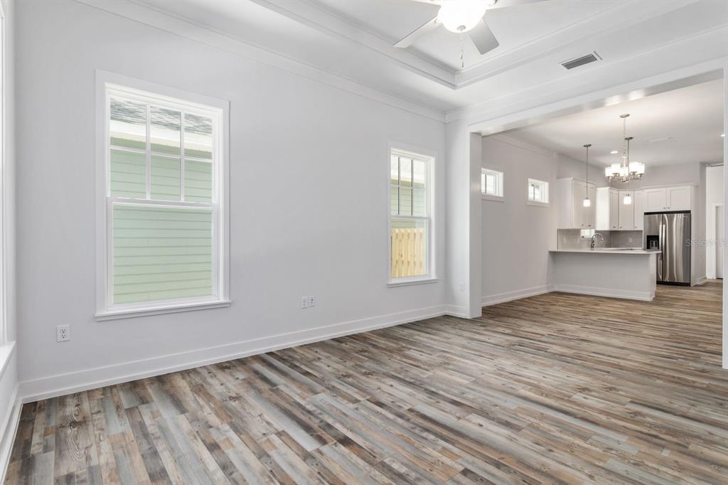 An empty living room with wood-look flooring opens into a kitchen with white cabinetry — 420 NW 1ST STREET, GAINESVILLE, FL