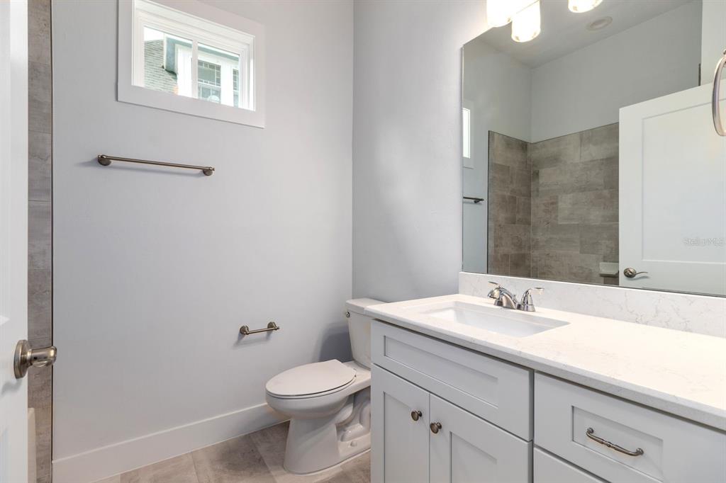 A bathroom with a white vanity, a toilet, a mirror, and gray tiled shower walls — 420 NW 1ST STREET, GAINESVILLE, FL
