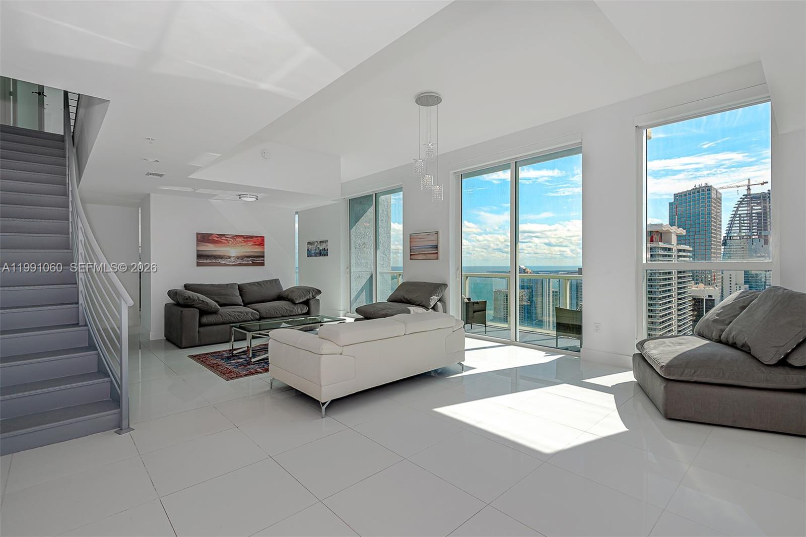 A modern living room features white tile floors, a staircase, and floor-to-ceiling windows with views — 244 Biscayne Blvd # 4907, Miami FL 33132, MIAMI, FL
