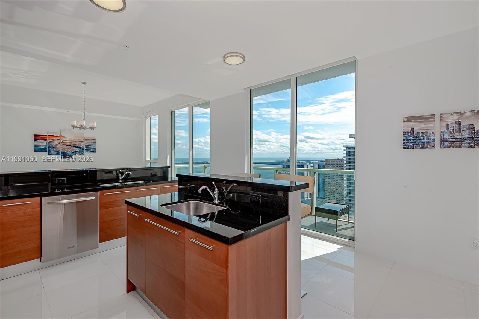 A modern kitchen features wood cabinets, black countertops, stainless steel appliances, and floor-to-ceiling windows — 244 Biscayne Blvd # 4907, Miami FL 33132, MIAMI, FL