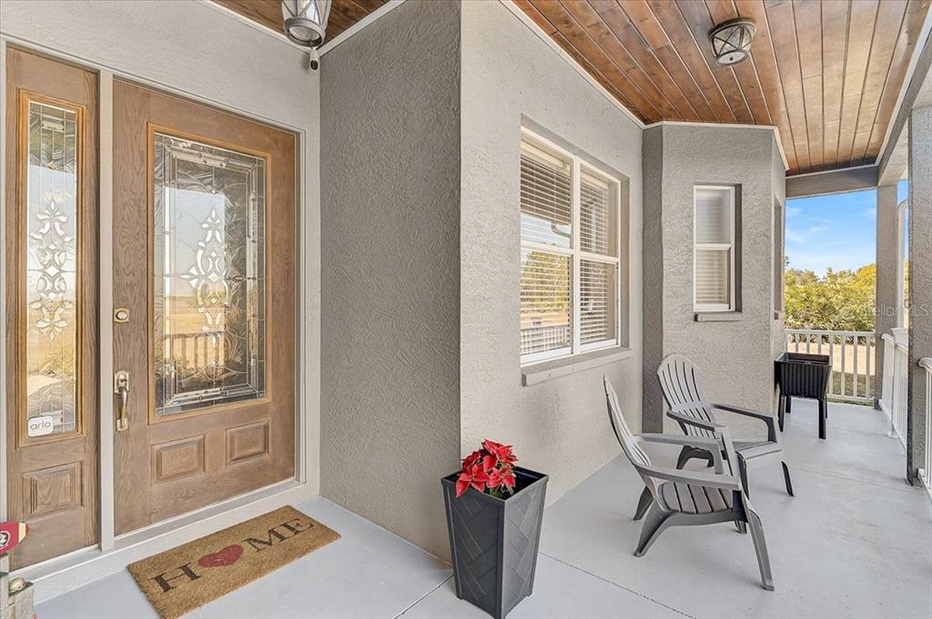 A covered front porch features a wooden door with glass panels and two gray chairs — 25202 E 61ST AVENUE, MYAKKA CITY, FL