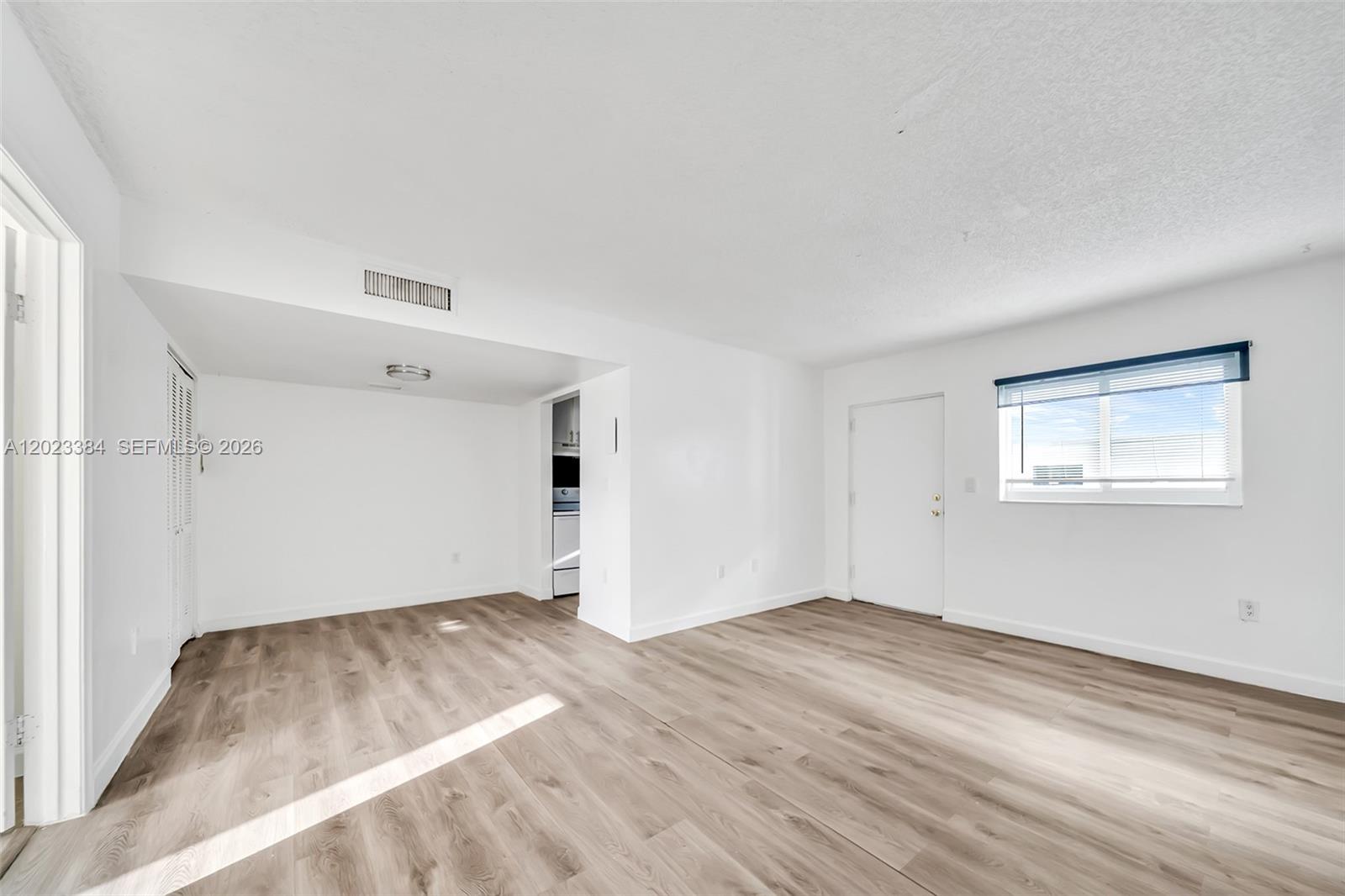 An empty room features white walls, light wood-look flooring, a window, and a doorway — 2011 Bay Dr # 8, Miami Beach FL 33141, MIAMI BEACH, FL