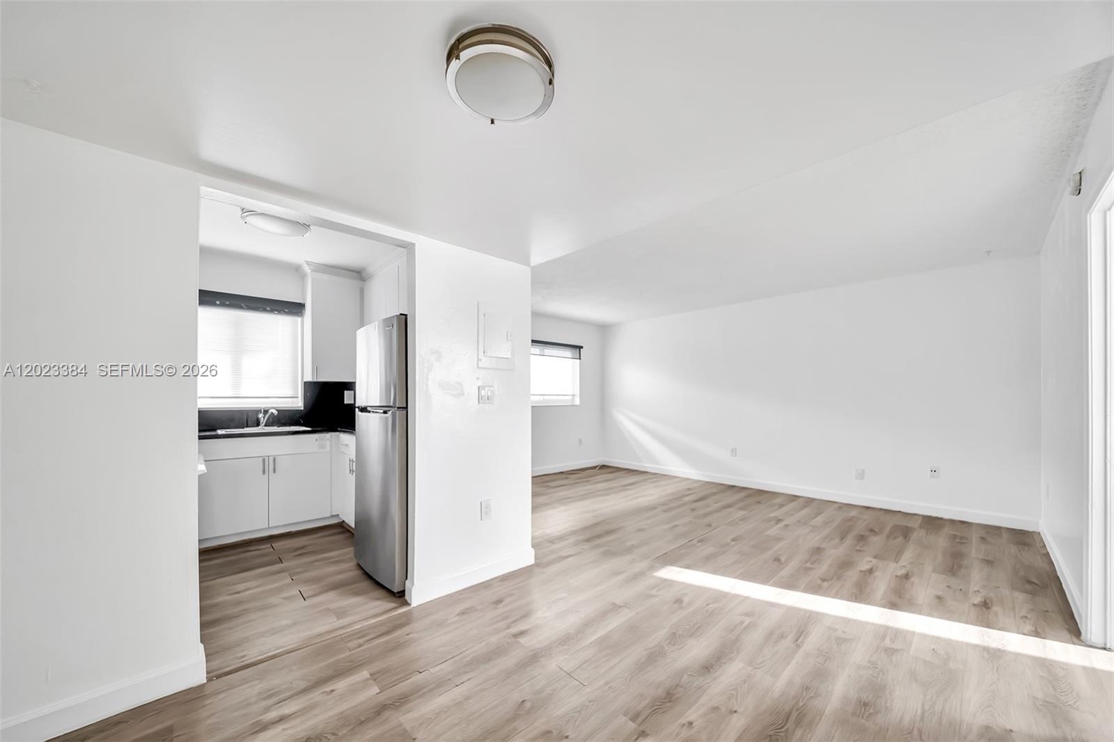 An open-concept living area features light wood-look flooring and a small adjacent kitchen with white cabinets — 2011 Bay Dr # 8, Miami Beach FL 33141, MIAMI BEACH, FL