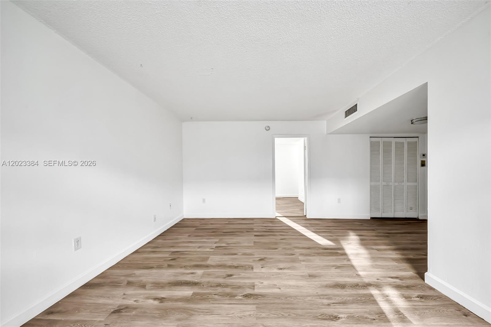An empty room features white walls, wood-look flooring, and a doorway leading to another space — 2011 Bay Dr # 8, Miami Beach FL 33141, MIAMI BEACH, FL