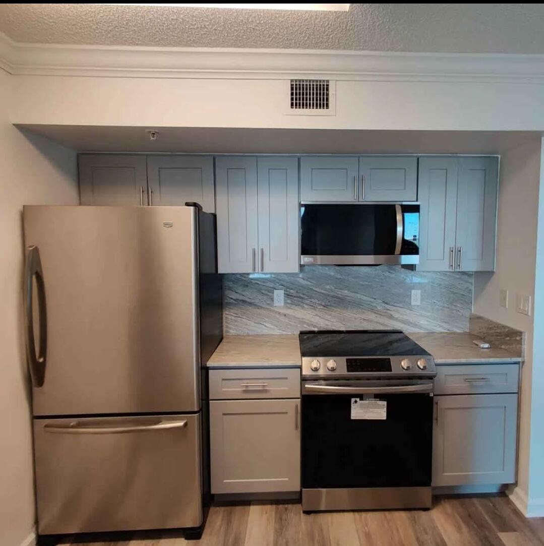 A kitchen features light gray cabinets, stainless steel appliances, and a stone-patterned backsplash — 1000 Scotia Drive # 506, Hypoluxo FL 33462, HYPOLUXO, FL