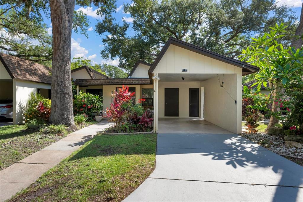 A single-story house with a carport, a concrete driveway, and lush landscaping under large trees — 2227 CIRCLEWOOD DRIVE UNIT 52, SARASOTA, FL