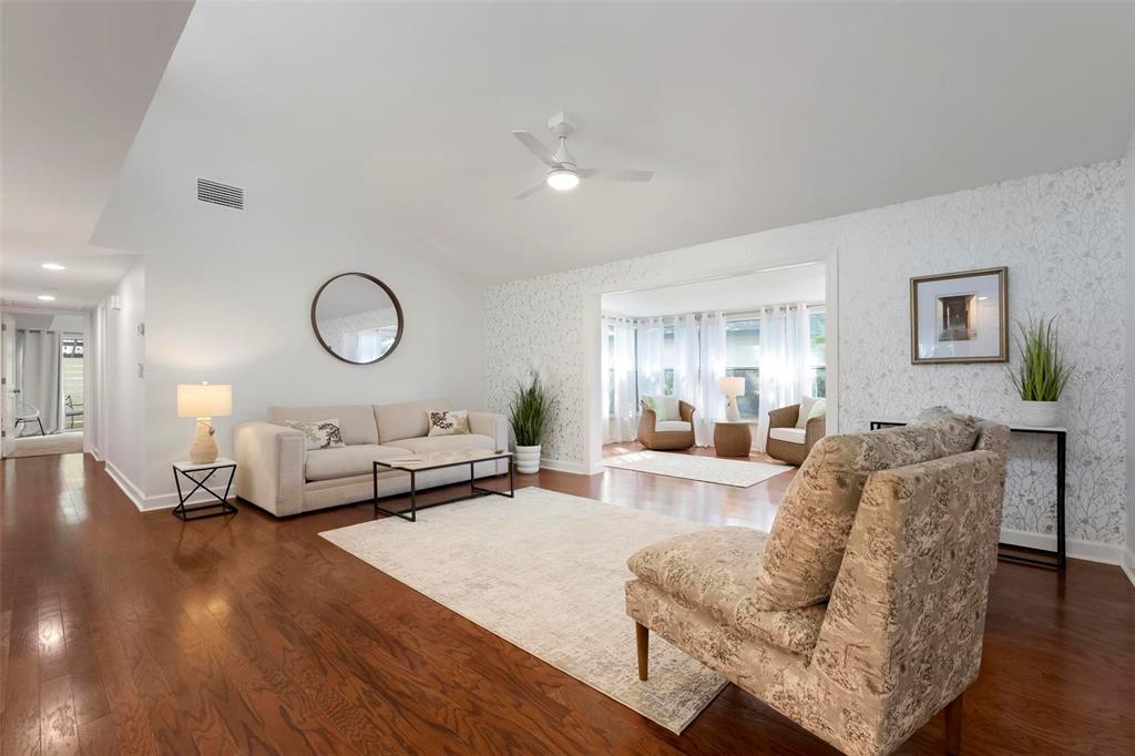 A living room features hardwood floors, a vaulted ceiling, a sofa, and a sunroom beyond — 2227 CIRCLEWOOD DRIVE UNIT 52, SARASOTA, FL