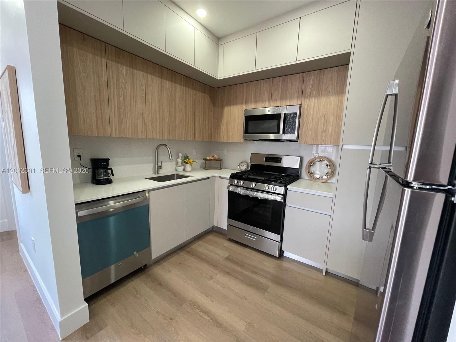 A modern kitchen features two-toned cabinetry, stainless steel appliances, and light wood-look flooring — 1619 Jefferson Ave # 201, Miami Beach FL 33139, MIAMI BEACH, FL