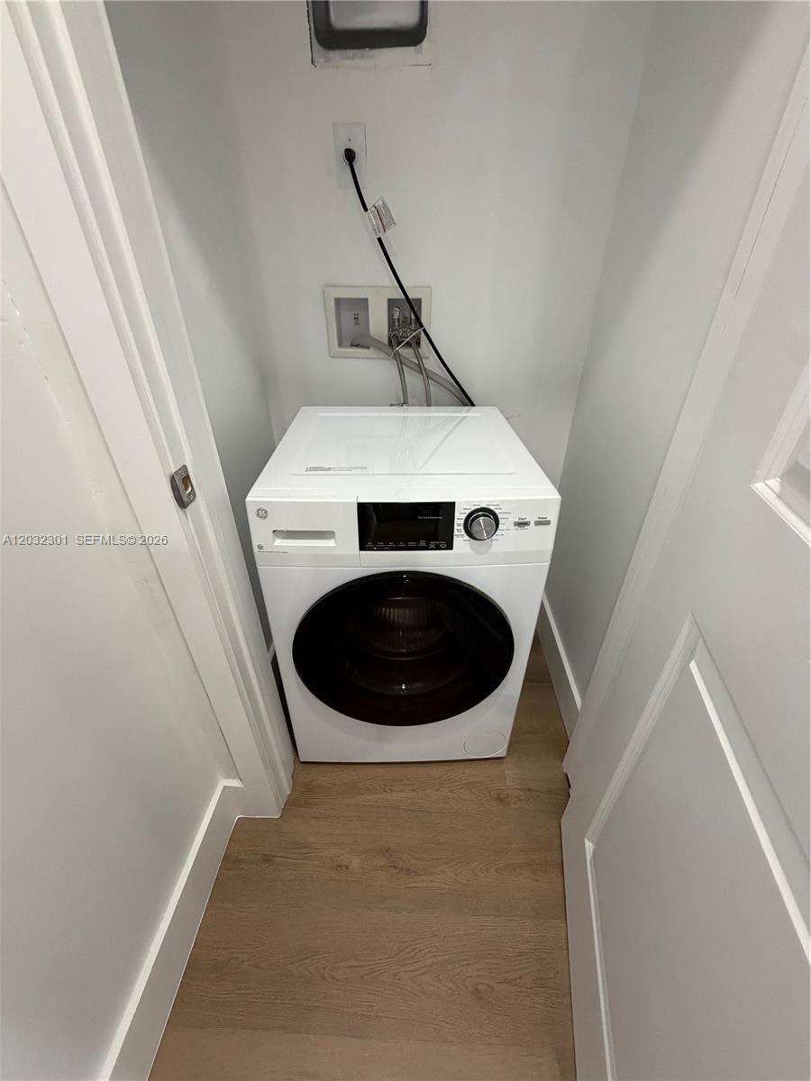 A white front-load washing machine is installed in a small laundry closet with wood flooring — 1619 Jefferson Ave # 201, Miami Beach FL 33139, MIAMI BEACH, FL