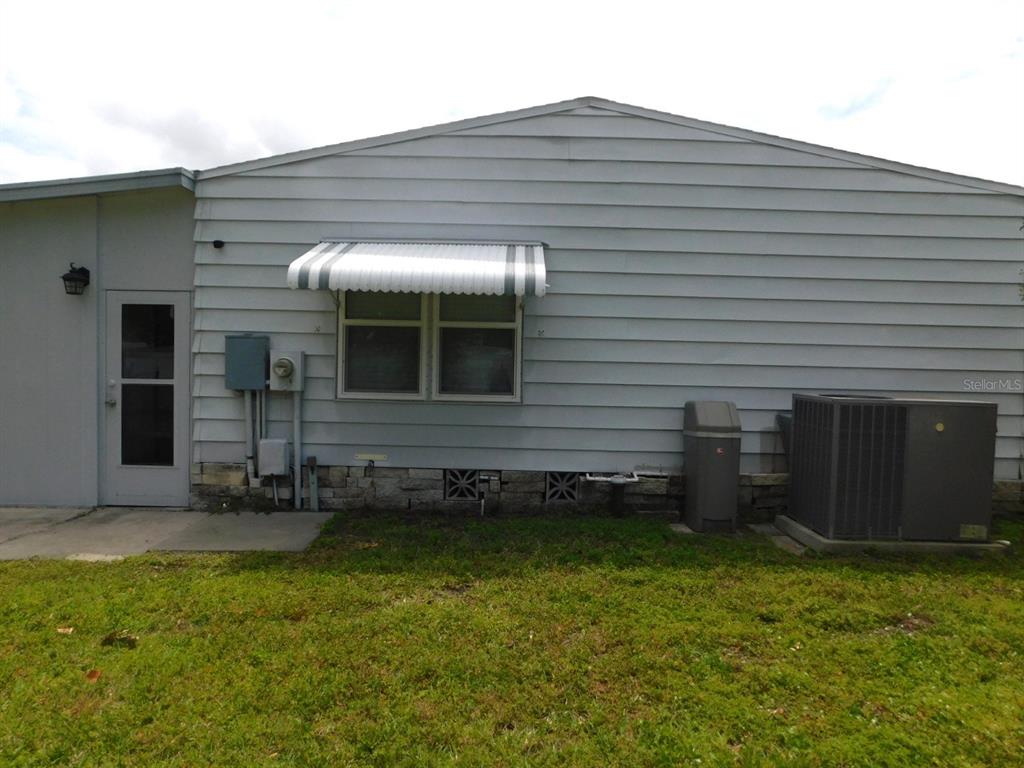 The exterior of a house features light gray siding, a window with an awning, and HVAC — 1001 STARKEY ROAD UNIT 99, LARGO, FL