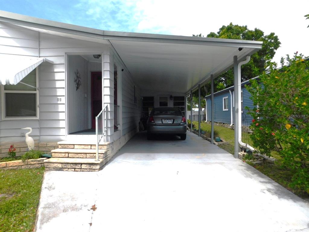 A white mobile home features a covered carport with a parked car and stone steps — 1001 STARKEY ROAD UNIT 99, LARGO, FL