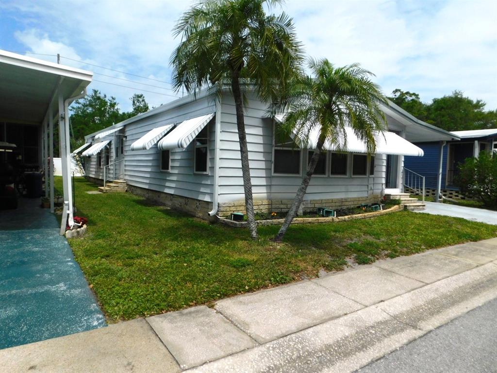 A light-colored mobile home with metal awnings and palm trees sits on a grassy lot — 1001 STARKEY ROAD UNIT 99, LARGO, FL