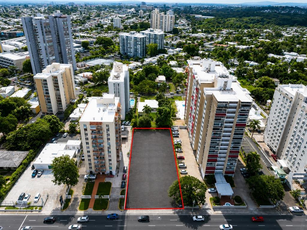 An aerial view shows a vacant rectangular paved lot situated between two high-rise apartment buildings — carr. 2 KM 6.4 VILLA CAPARRA, GUAYNABO, PR