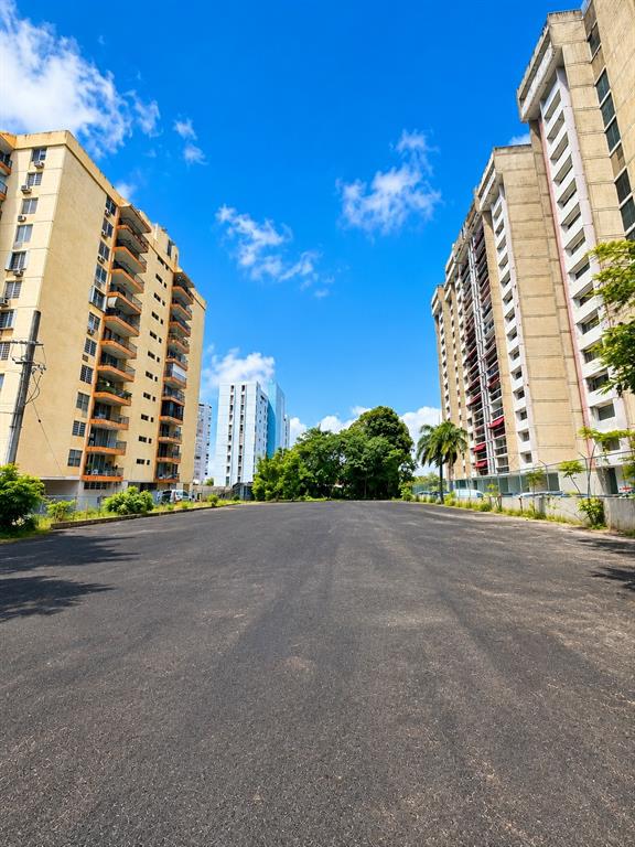 A paved lot sits between two tall apartment buildings under a bright blue sky — carr. 2 KM 6.4 VILLA CAPARRA, GUAYNABO, PR