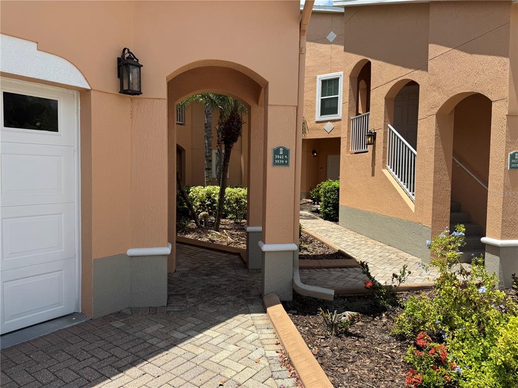 A paved walkway leads through an arched entryway between two peach-colored stucco residential buildings — 3939 SERENADE LANE UNIT 513, LAKELAND, FL